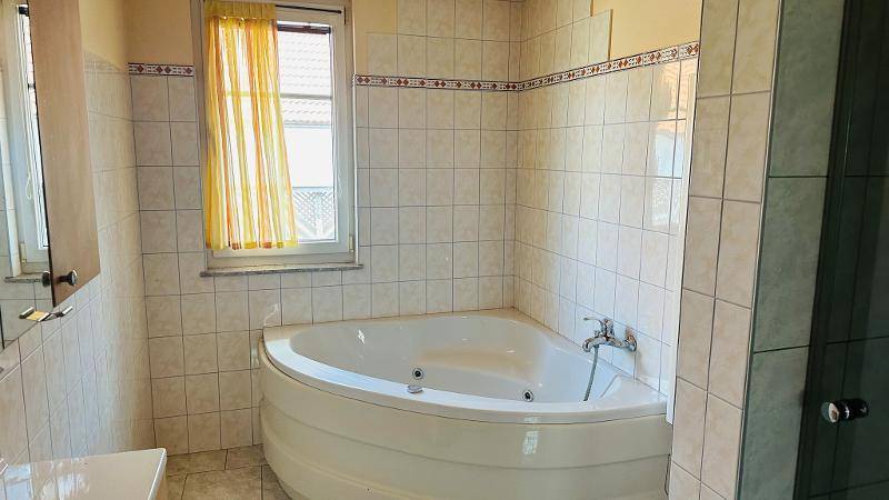 Badezimmer mit Eckbadewanne, Fliesenwänden und Fenster.