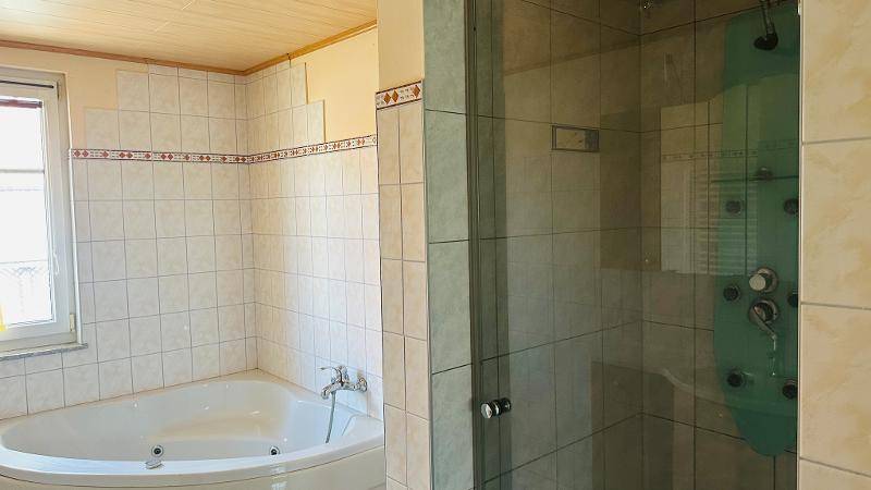 Badezimmer mit Eckbadewanne, Duschkabine und Fliesenwänden.