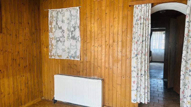 Rustikaler Raum mit Holzvertäfelung, Fenster und Heizkörper.