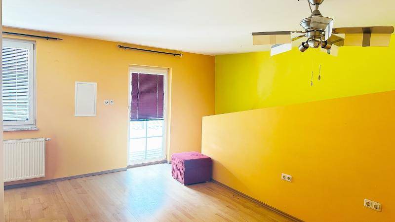 Helles Zimmer mit gelben Wänden, Holzfußboden und Deckenventilator.