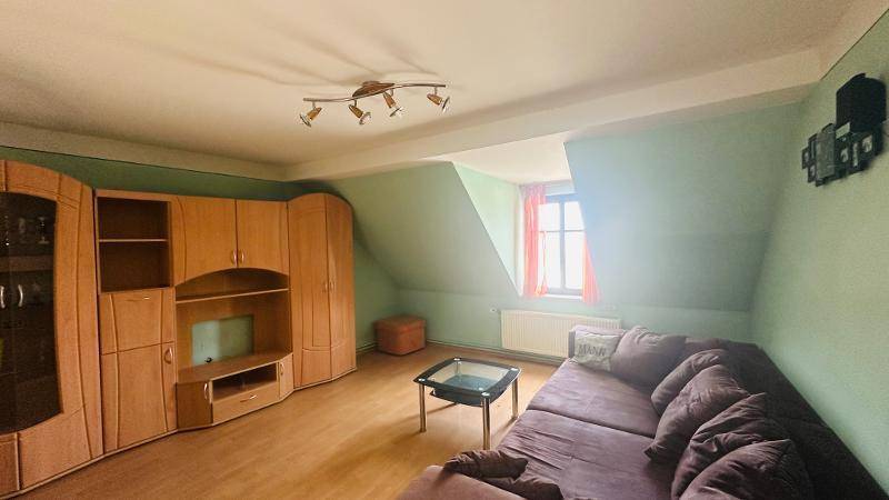 Gemütliches Wohnzimmer im Dachgeschoss mit Schrägen, Sofa und Holzmöbeln.