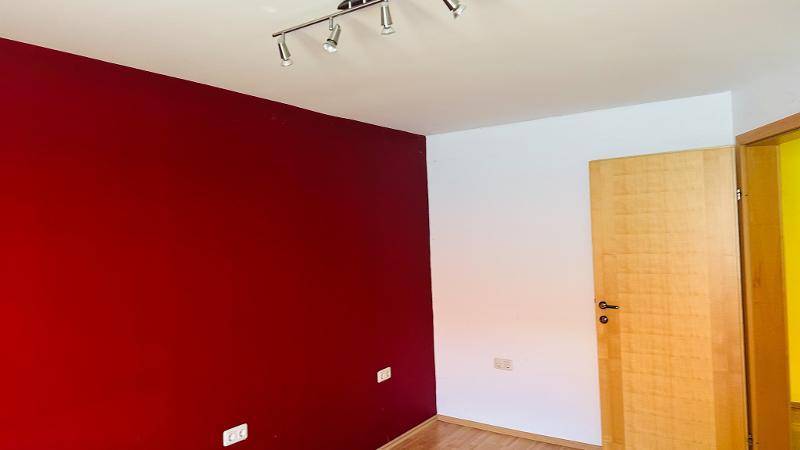 Schlafzimmer mit roter Akzentwand, Holzfußboden und Holztür.