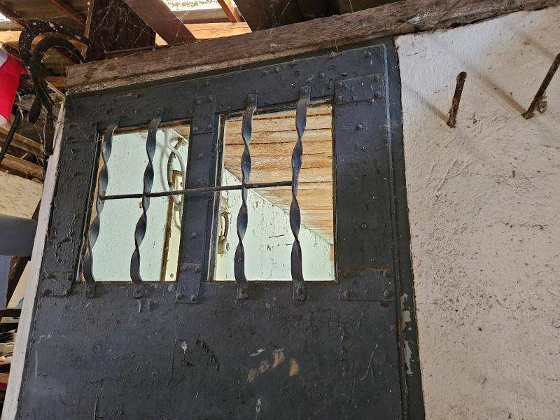 Alte, robuste Holztür mit schmiedeeisernen Gittern und kleinen Fenstern in einem rustikalen Innenraum.