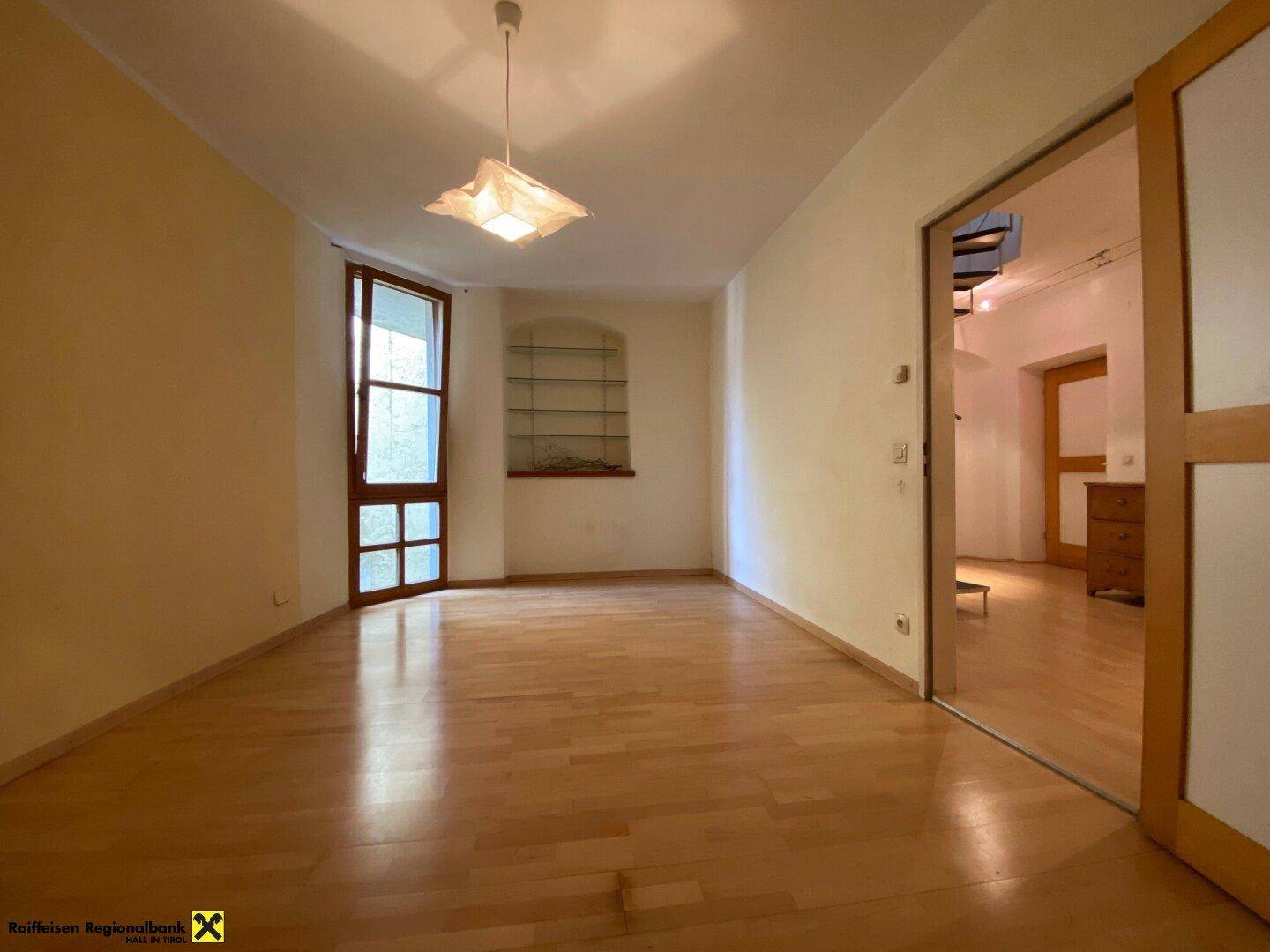 Heller, leerer Raum mit Holzboden und einem Fenster, das viel Tageslicht hereinlässt.