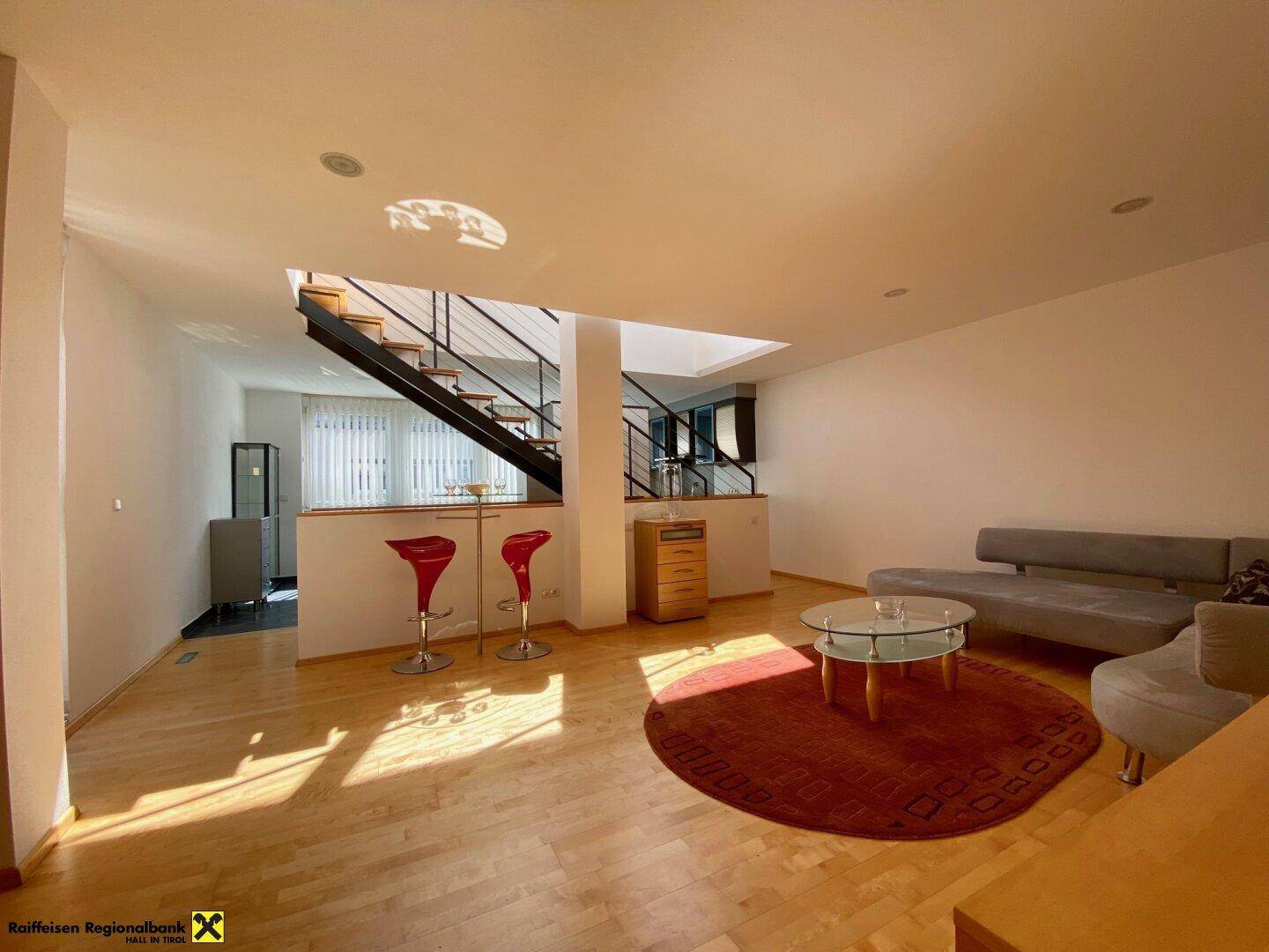Geräumiges Wohnzimmer mit Holzboden, moderner Einrichtung und Zugang zur Treppe.