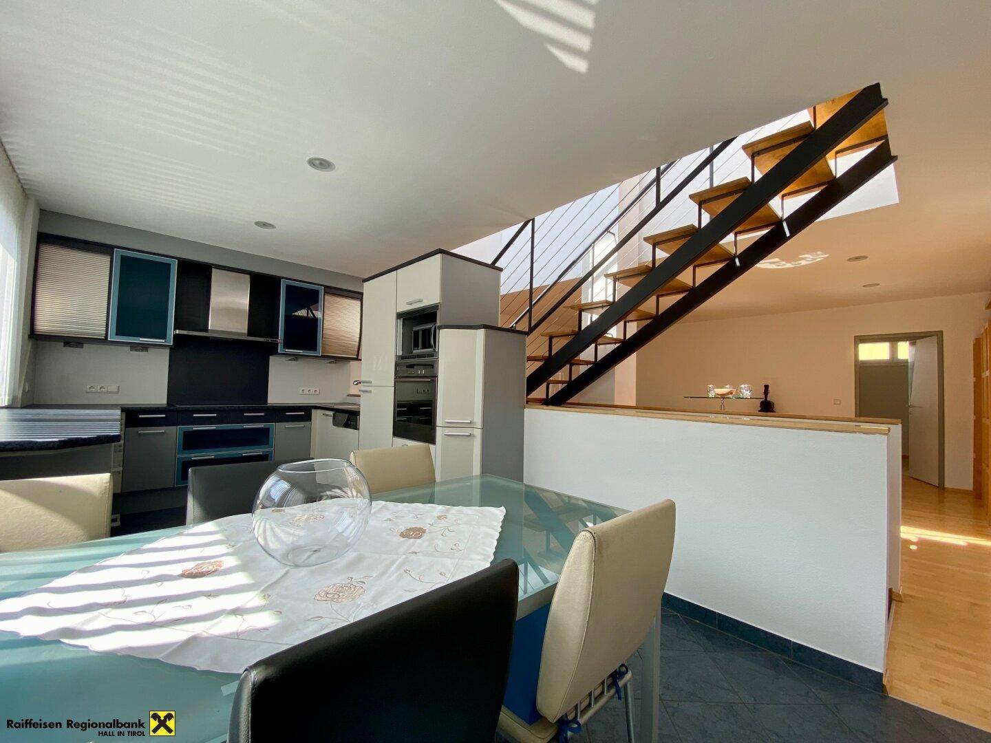 Moderne Küche mit Essbereich, Einbaugeräten und Blick auf die offene Treppe.