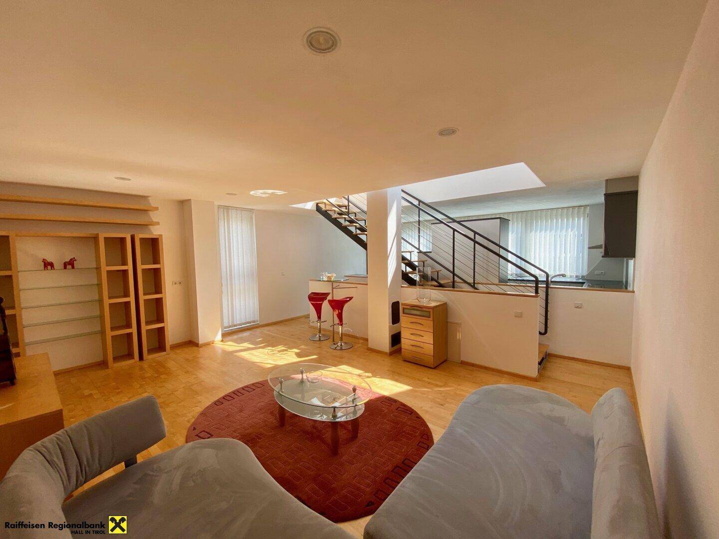 Helles Wohnzimmer mit Holzfußboden, bequemen Sofas und offener Treppe.