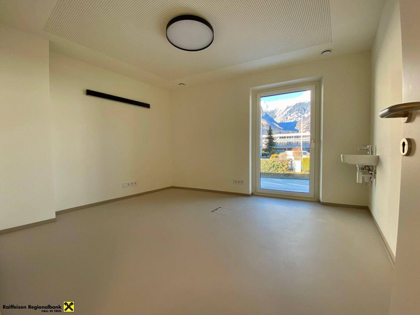 Heller Raum mit einem Waschbecken, großem Fenster und Blick auf die umliegende Landschaft und Berge.