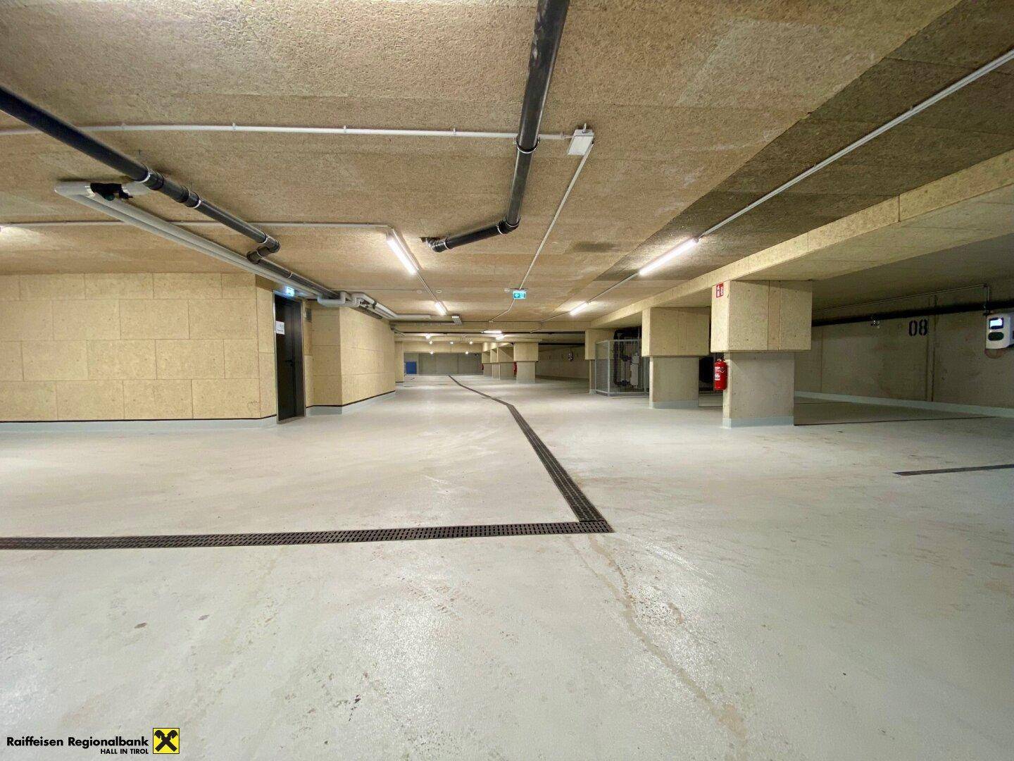 Geräumige Tiefgarage mit hellem Betonboden, sichtbaren Leitungen und effizienter Deckenbeleuchtung.