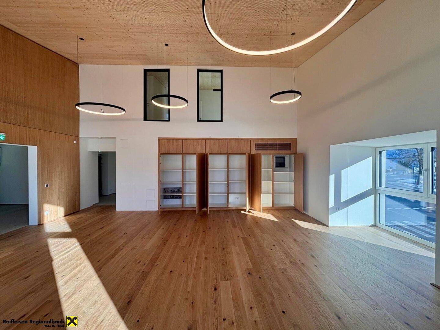 Heller, offener Raum mit Holzboden und eingebauten Regalen, durchflutet von natürlichem Licht durch große Fenster.