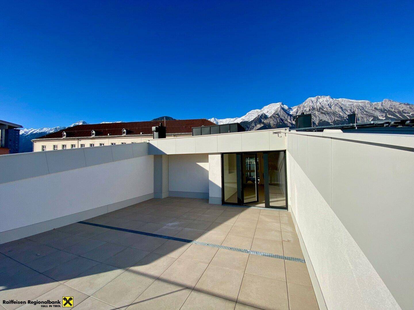 Große Dachterrasse mit Fliesenboden und weitem Blick auf die schneebedeckten Berge unter strahlend blauem Himmel.