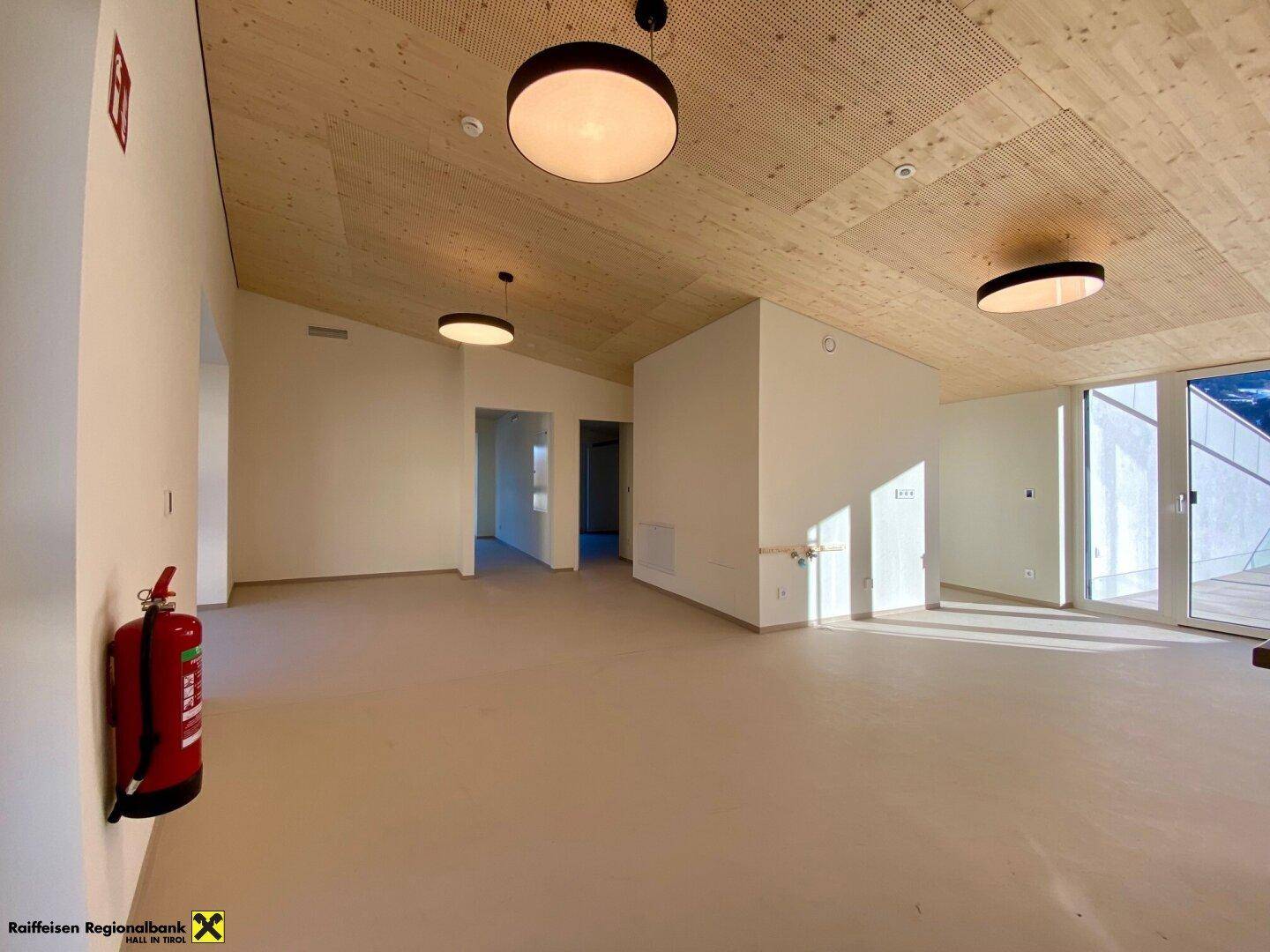 Heller, leerer Raum mit hohen Decken, Holzakustikplatten und großen Fenstern, die viel Tageslicht hereinlassen.