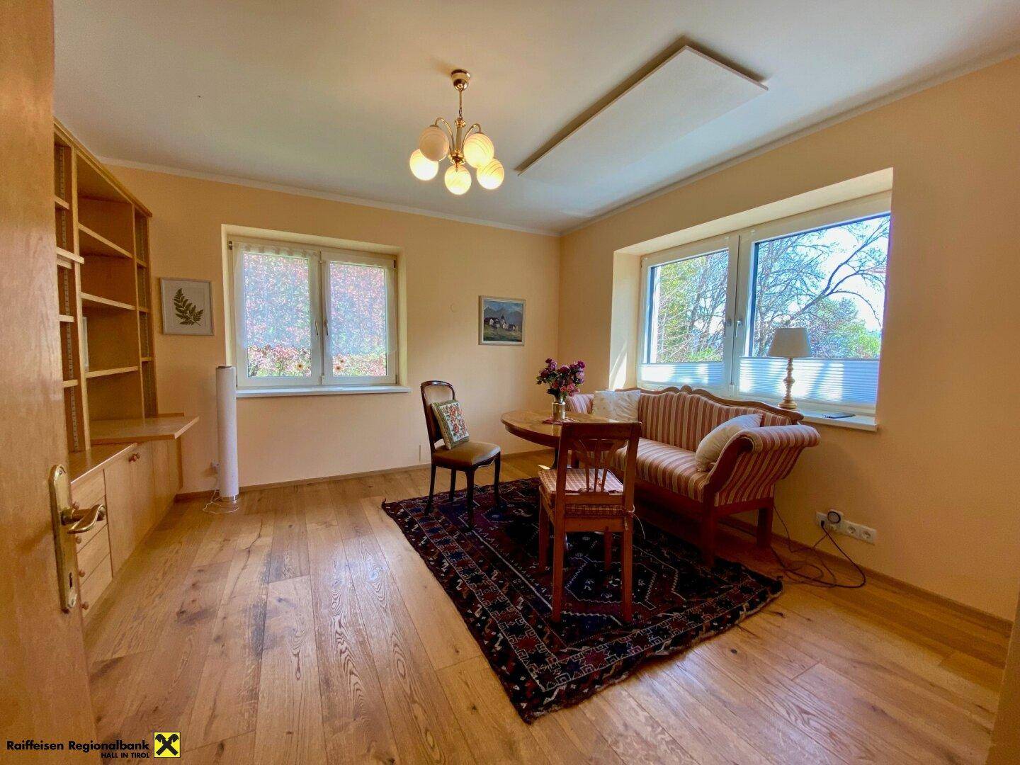 Gemütliches Wohnzimmer mit Holzboden, großen Fenstern und traditionellen Möbeln.