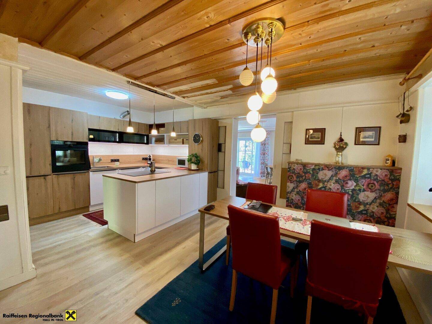 Moderne Küche mit Holzakzenten, Kochinsel und Essbereich unter einer Holzdecke.