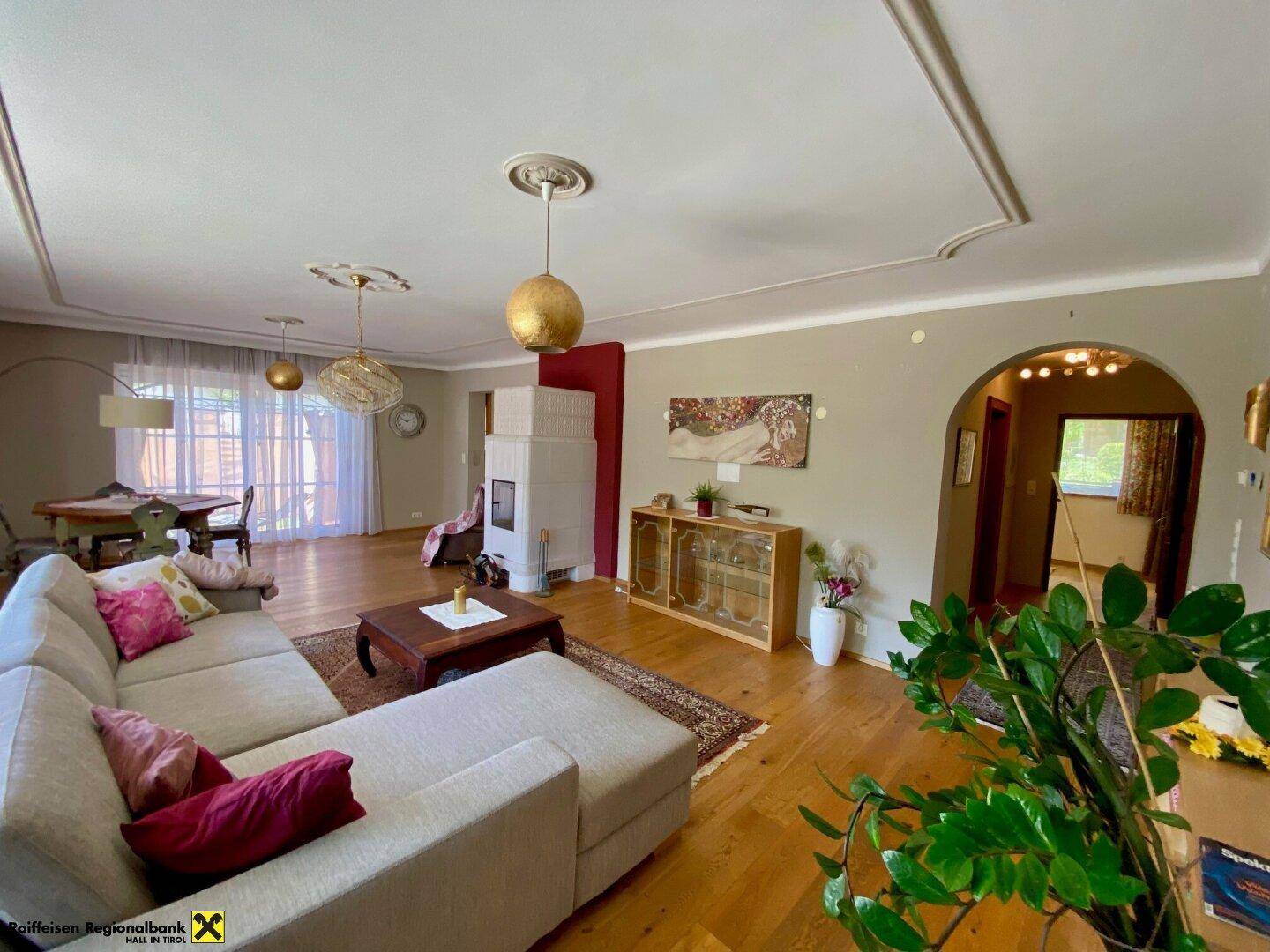Helles Wohn- und Esszimmer mit Holzboden, Stuckdecken und einem traditionellen Kachelofen.