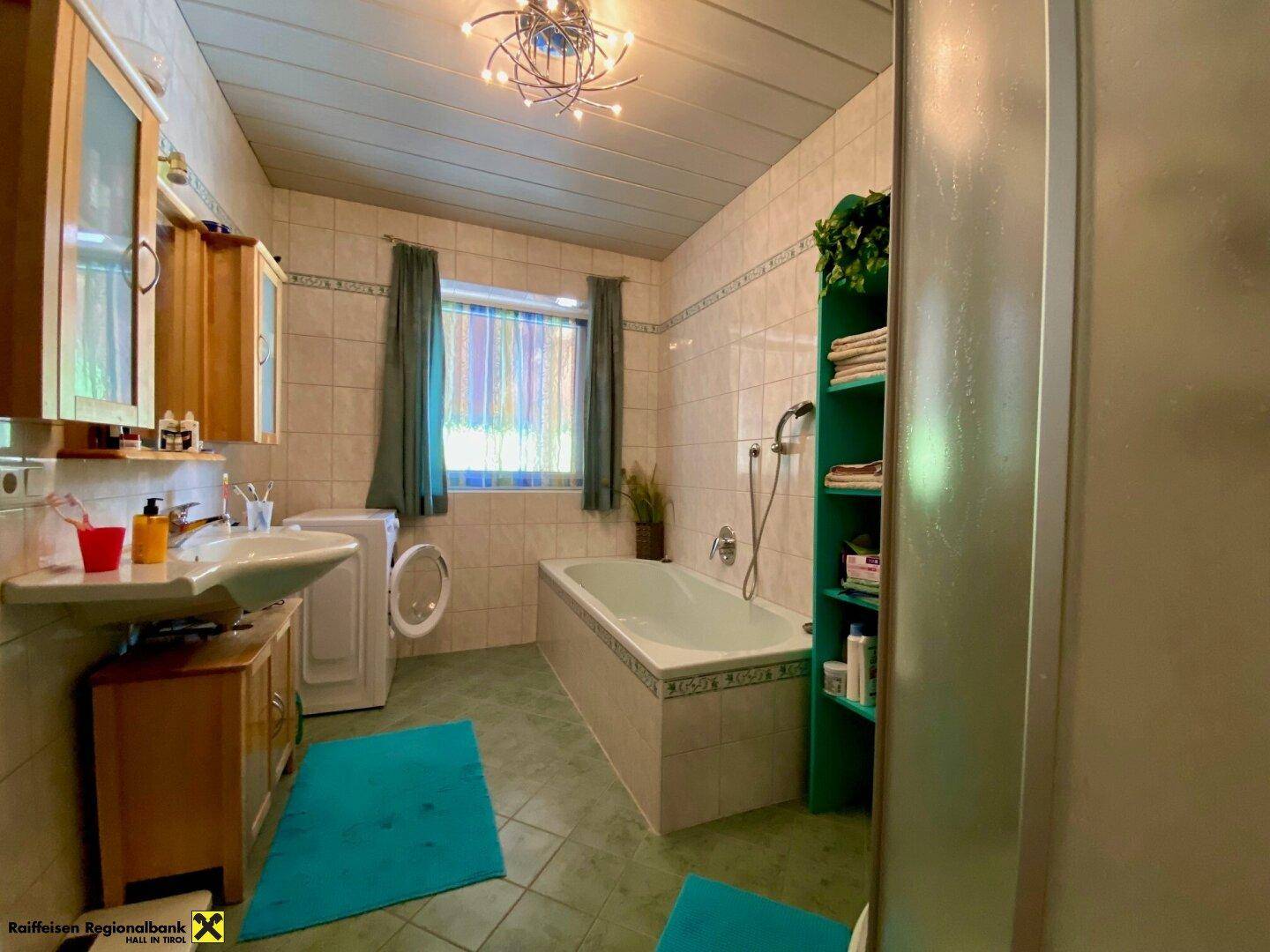 Badezimmer mit Badewanne, Waschbecken und Waschmaschine in funktionaler Ausstattung.