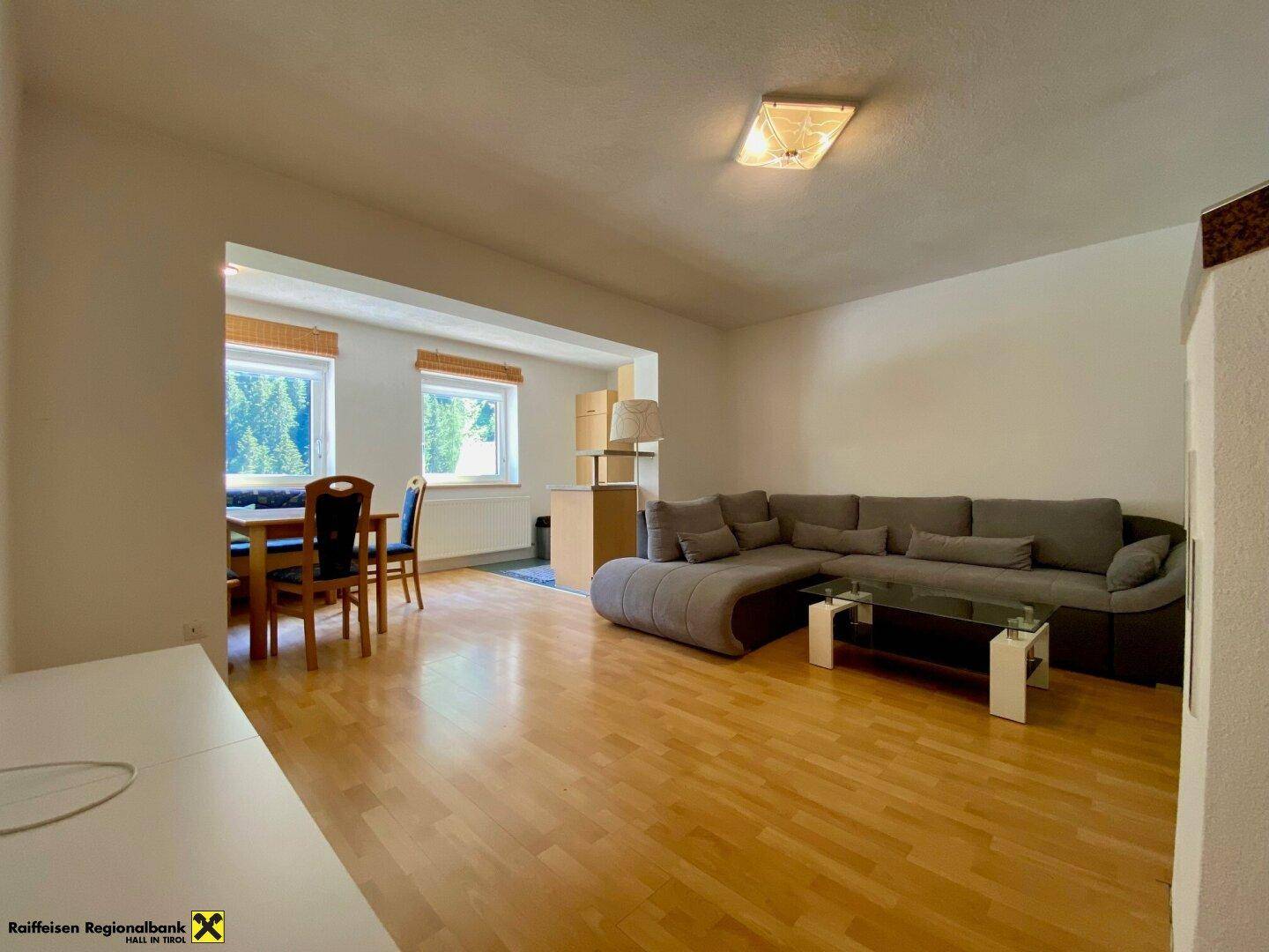 Geräumiger Wohn-Essbereich mit Holzboden, großer Couch und Essplatz am Fenster.