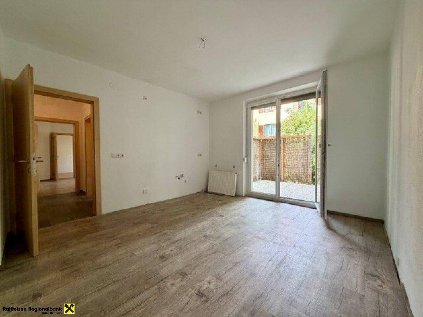Heller, leerer Raum mit Laminatboden und Zugang zu einer kleinen Terrasse.