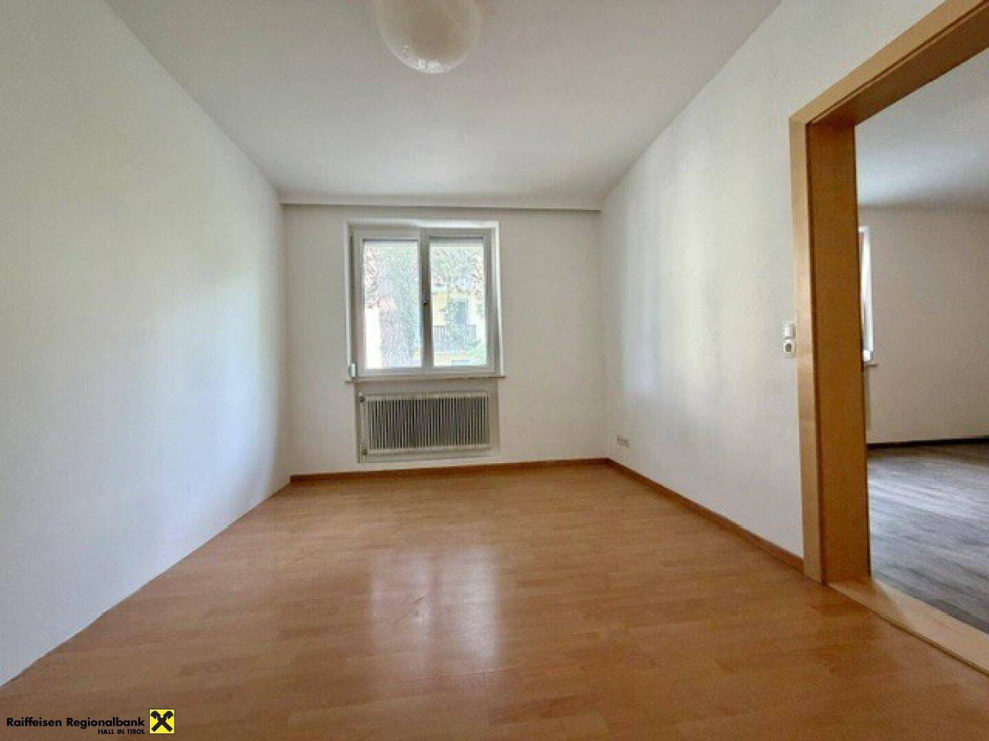 Geräumiges Schlafzimmer mit hellem Laminatboden und Fenster, das viel Tageslicht hereinlässt.