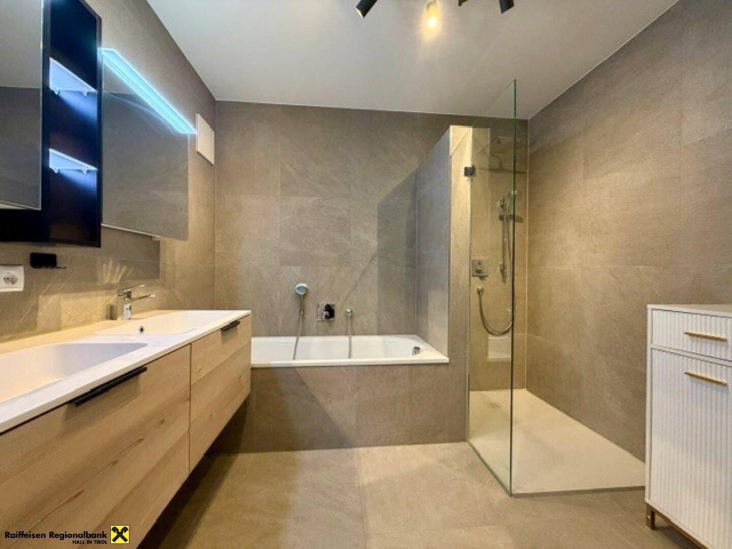 Modernes Badezimmer mit grauen Fliesen, Badewanne, begehbarer Dusche und Doppelwaschbecken.