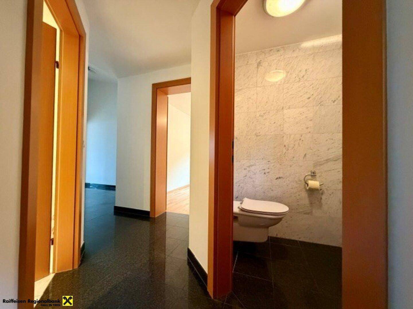 Flur mit dunklem Fliesenboden und Zugang zu verschiedenen Zimmern, inklusive einer separaten Gästetoilette.
