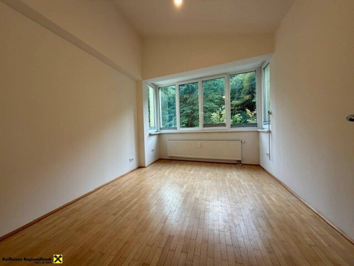 Geräumiges Schlafzimmer mit Holzboden und großer Fensterfront, die viel Tageslicht und Grünblick bietet.