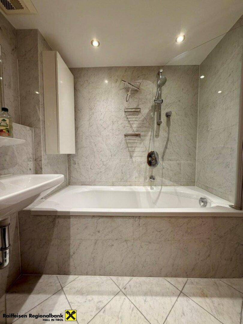 Modern gefliestes Badezimmer mit Badewanne und integrierter Dusche, ausgestattet mit einem Waschbecken.