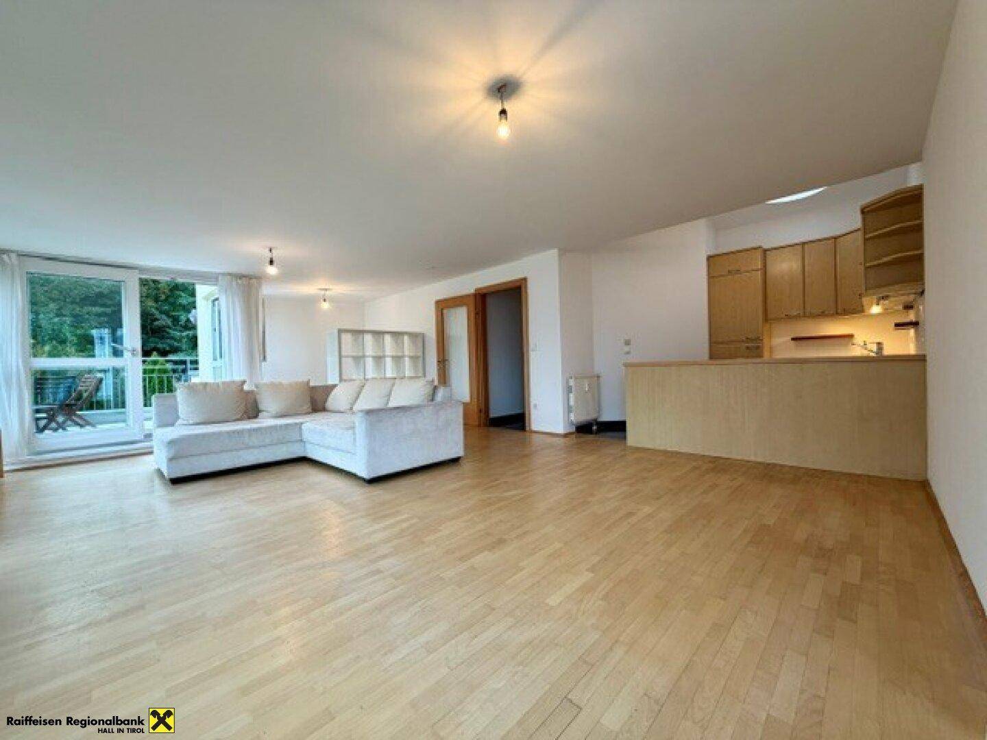 Heller offener Wohnbereich mit Holzboden und integrierter Küchenzeile, ideal für geselliges Beisammensein.