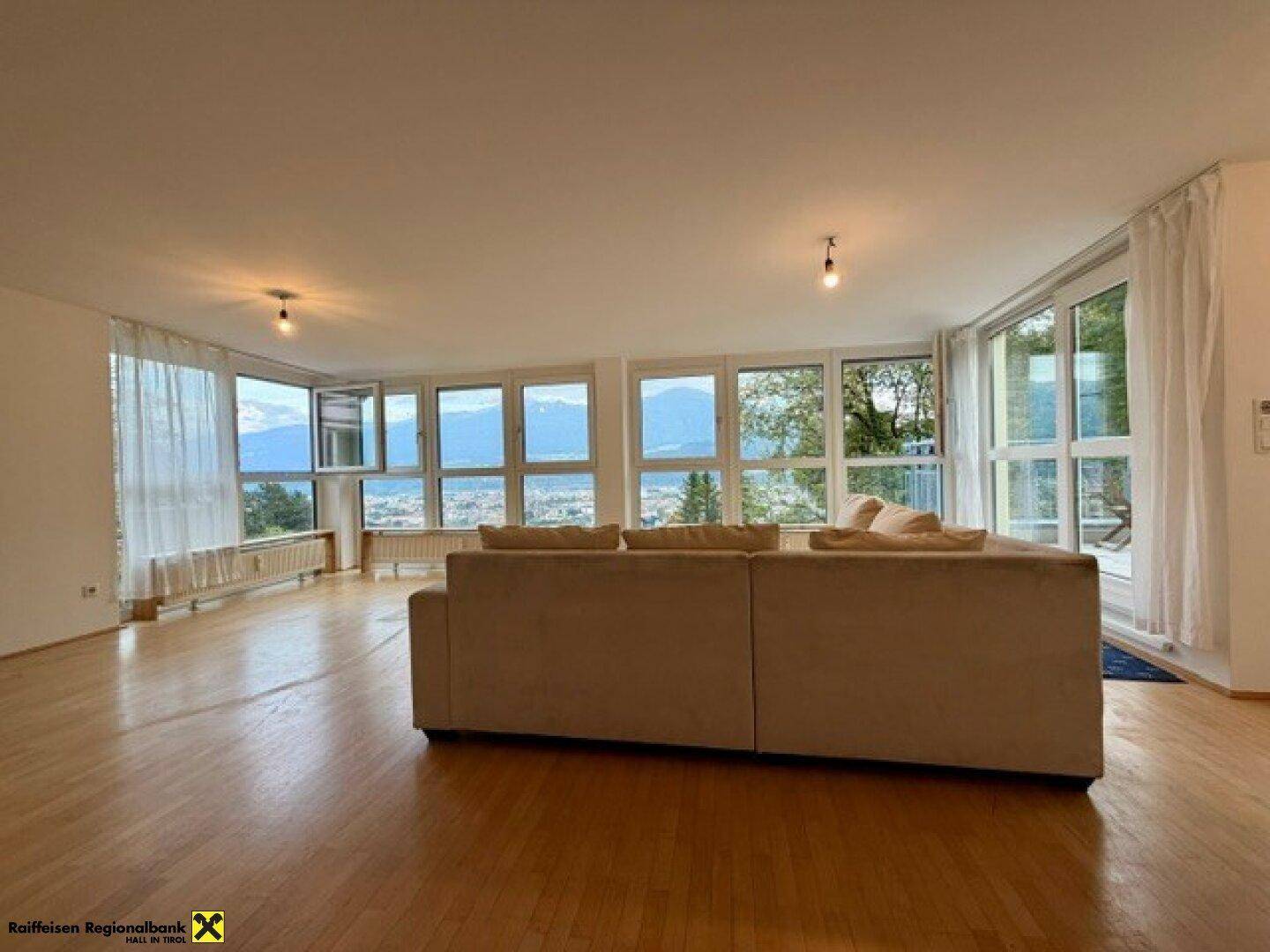 Lichtdurchflutetes Wohnzimmer mit Panoramablick auf die Stadt und die umliegende Bergwelt, ausgestattet mit Holzboden.