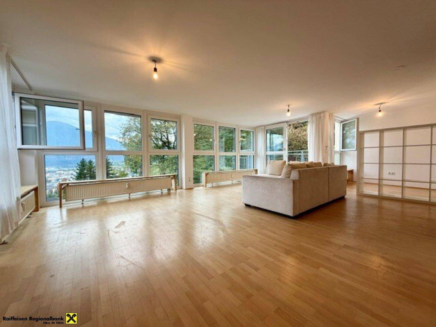 Großzügiges Wohnzimmer mit vielen Fenstern, die einen weiten Blick auf die Landschaft und die Berge bieten.