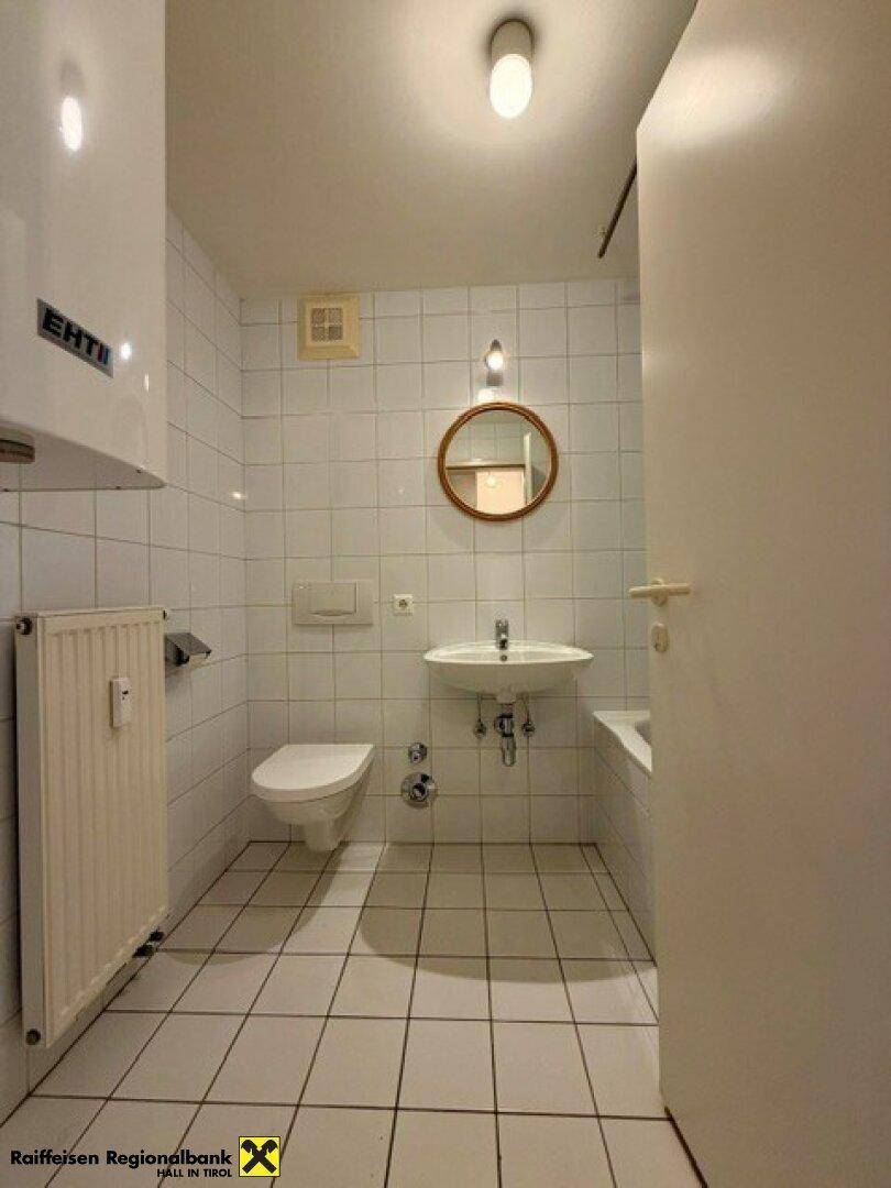 Funktionales Badezimmer mit weißen Fliesen, WC, Waschbecken und Heizkörper.