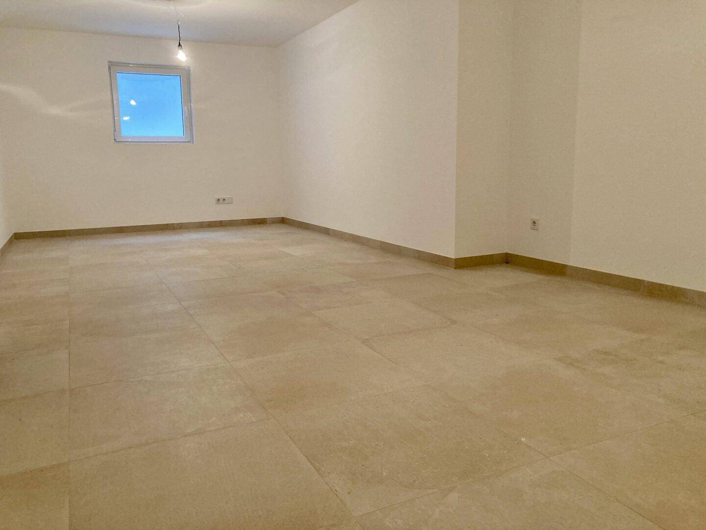 Leerer Raum mit Fliesenboden und einem kleinen Fenster, ideal für verschiedene Nutzungen.