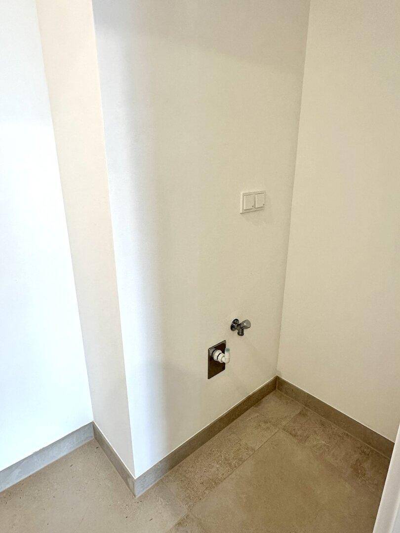Ecke eines Hauswirtschaftsraums mit Fliesenboden und Anschlüssen für eine Waschmaschine.