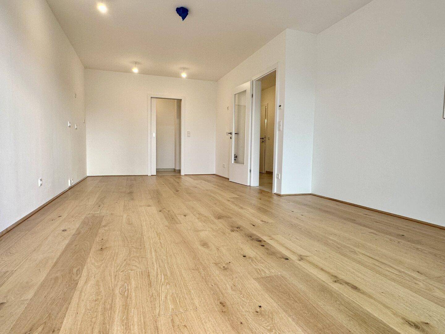Geräumiger, heller Raum mit neuem Holzparkettboden und weißen Wänden, bereit zur Einrichtung.