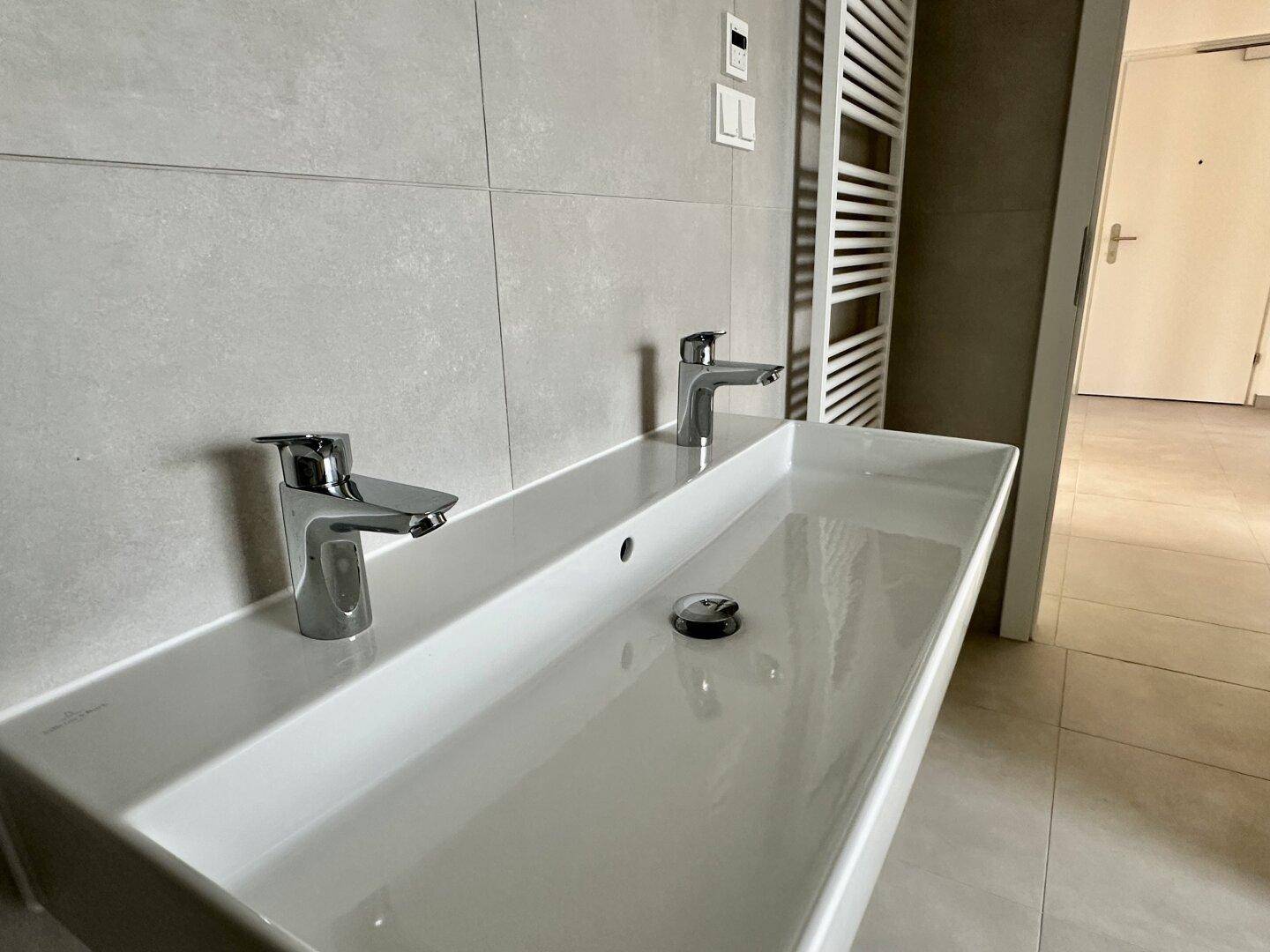 Modernes Badezimmer mit Doppelwaschbecken, eleganten Armaturen und beheiztem Handtuchhalter.