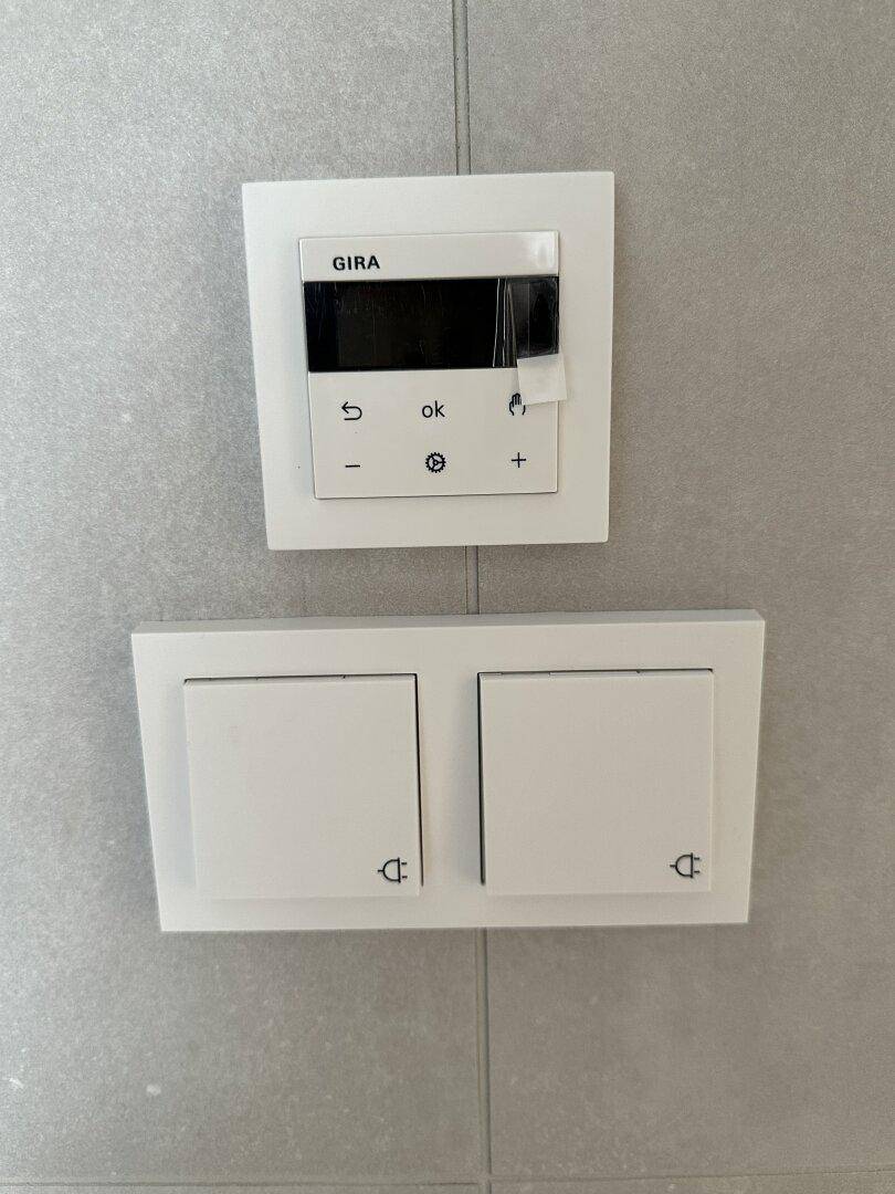 Moderne Lichtschalter und ein Thermostat der Marke GIRA an einer gefliesten Wand.