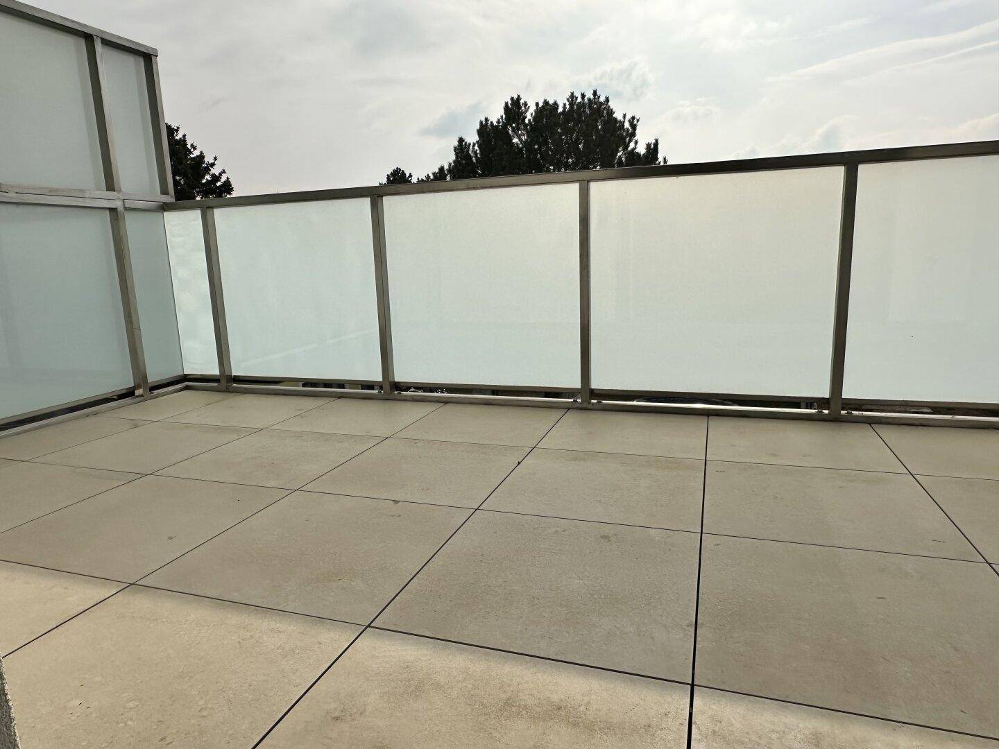 Moderner Balkon mit Fliesenboden und Milchglasgeländer, ideal für entspannte Stunden im Freien.