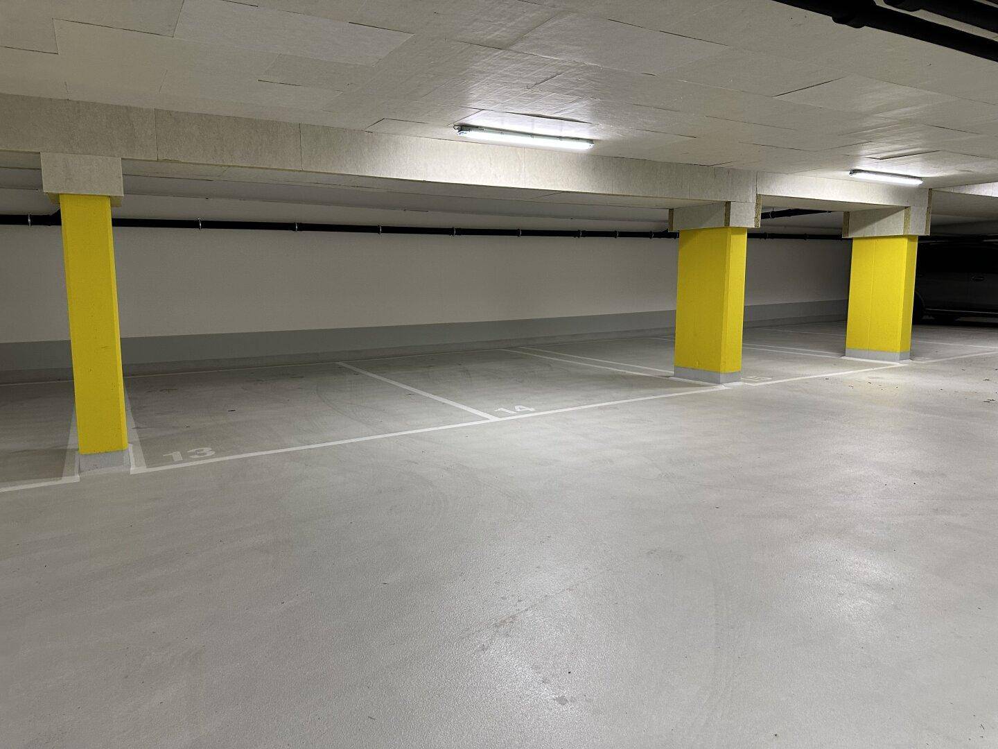 Geräumige Tiefgarage mit markierten Stellplätzen und leuchtend gelben Säulen.