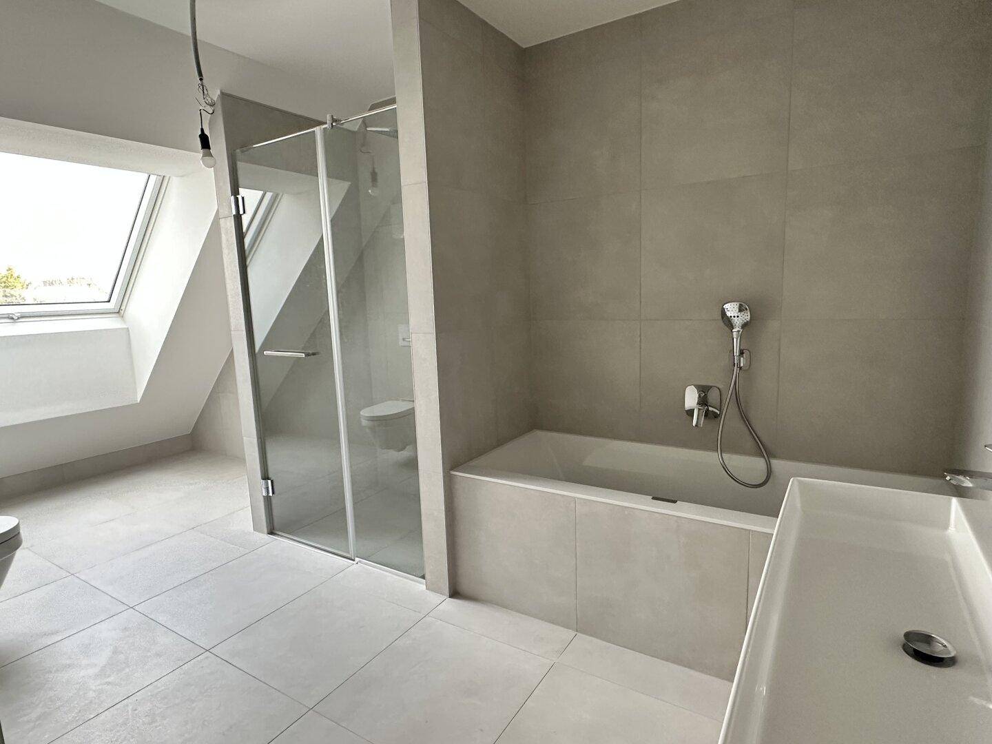 Modernes Badezimmer mit grauen Fliesen, Badewanne, begehbarer Dusche und Dachfenster.