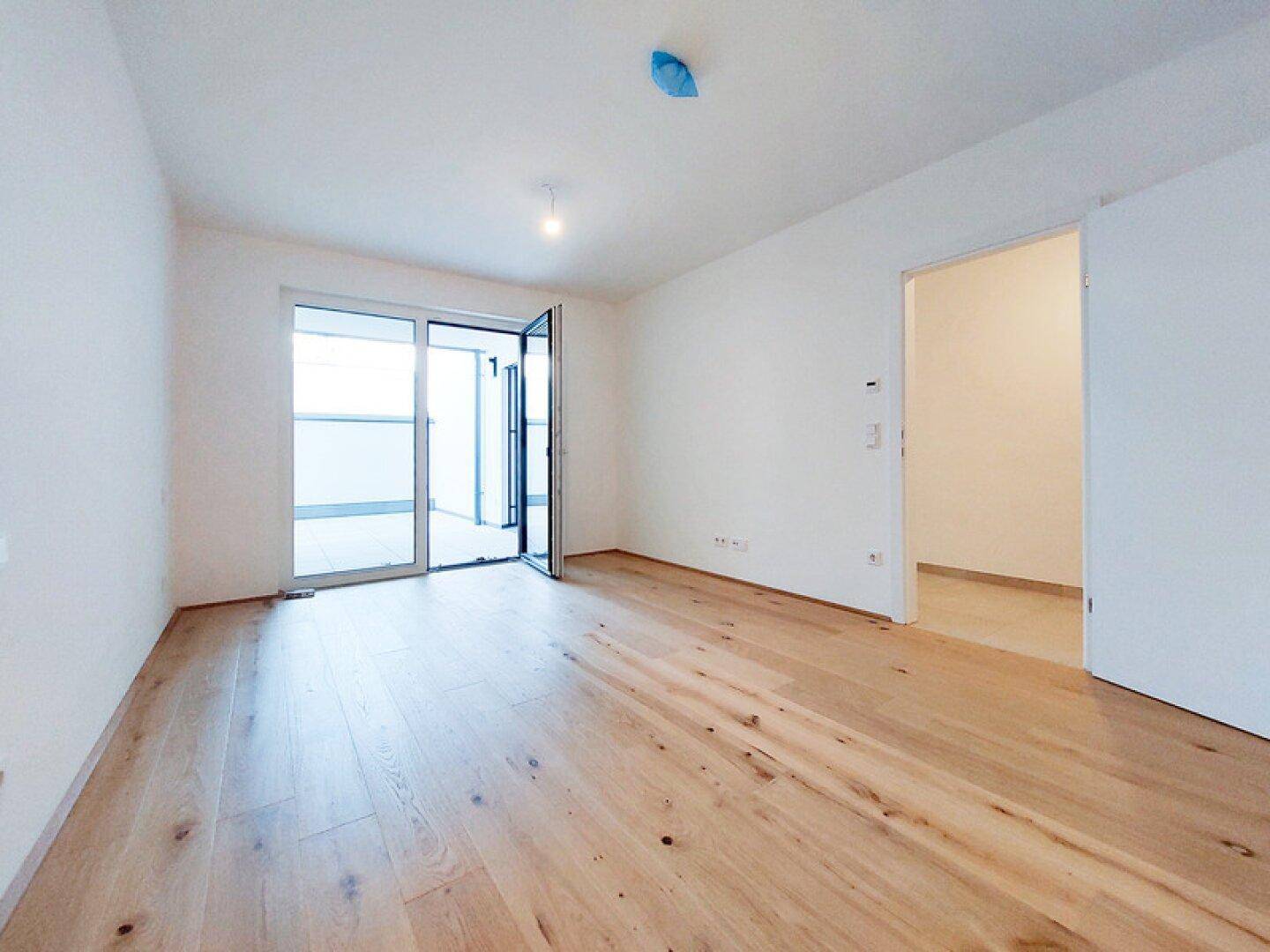 Geräumiger, heller Raum mit hellem Holzplankenboden und Zugang zum Balkon.