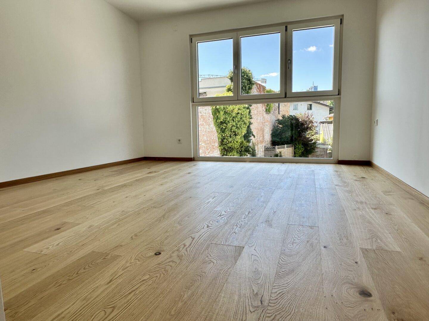 Geräumiger, heller Raum mit Holzboden und großer Fensterfront, die viel Tageslicht hereinlässt.