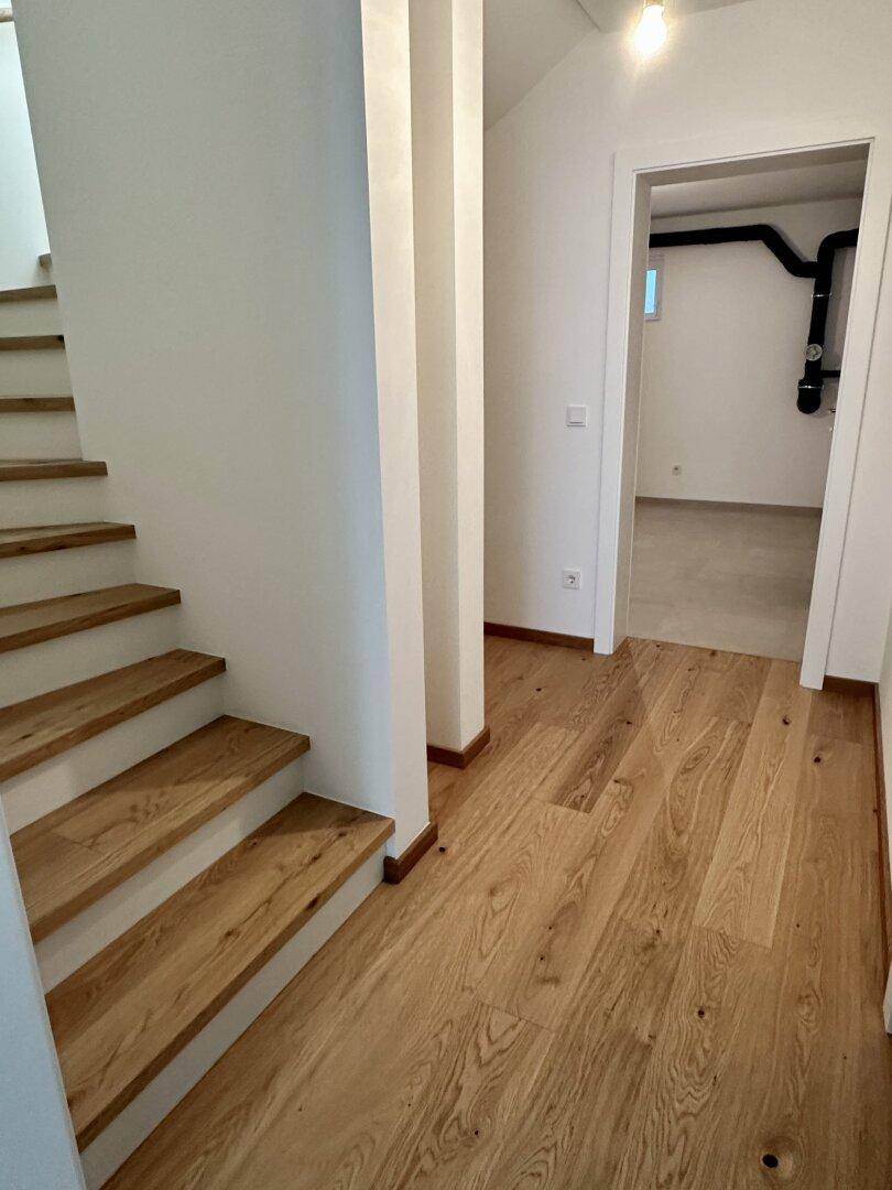 Heller Flur mit Holztreppe und passendem Parkettboden, der zu den oberen Etagen führt.