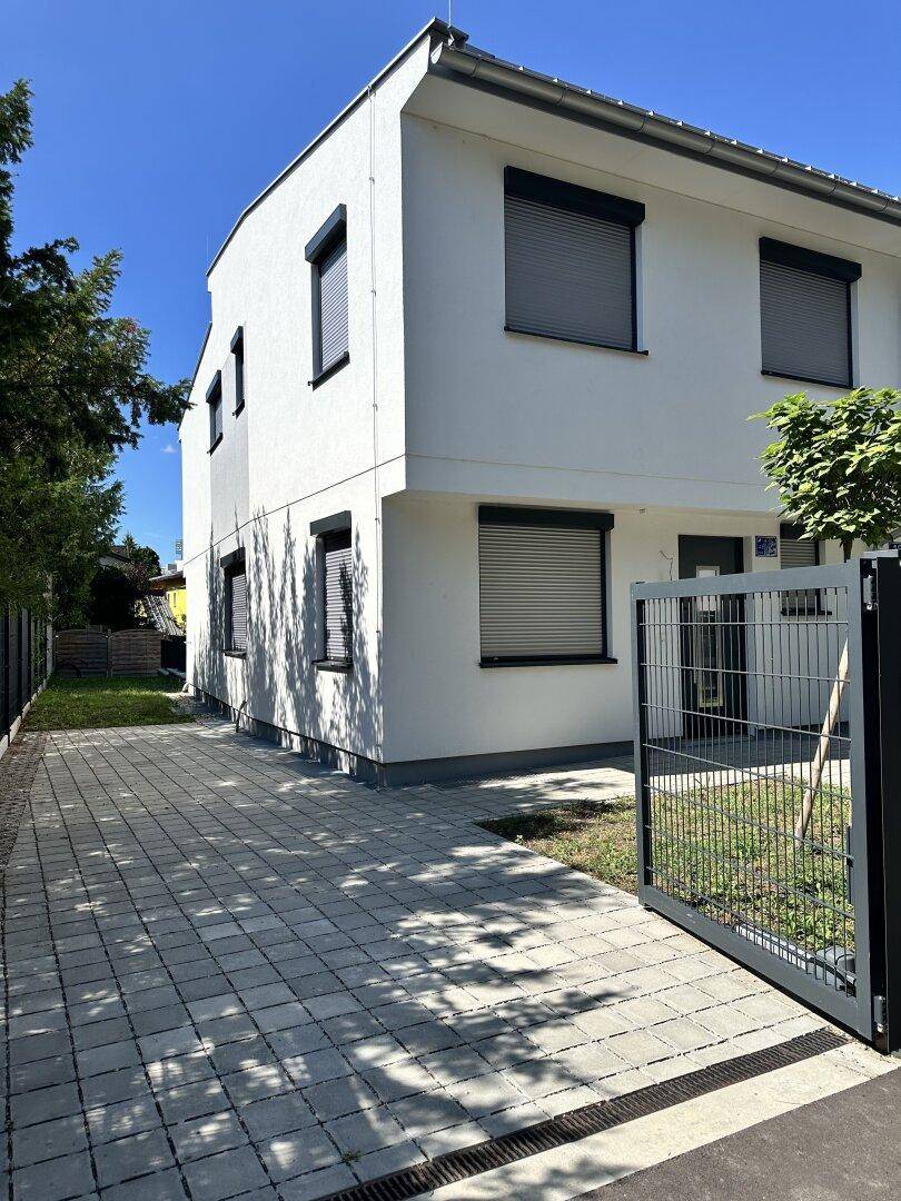 Moderne Doppelhaushälfte mit geschlossenen Rollläden und gepflegter Einfahrt an einem sonnigen Tag.