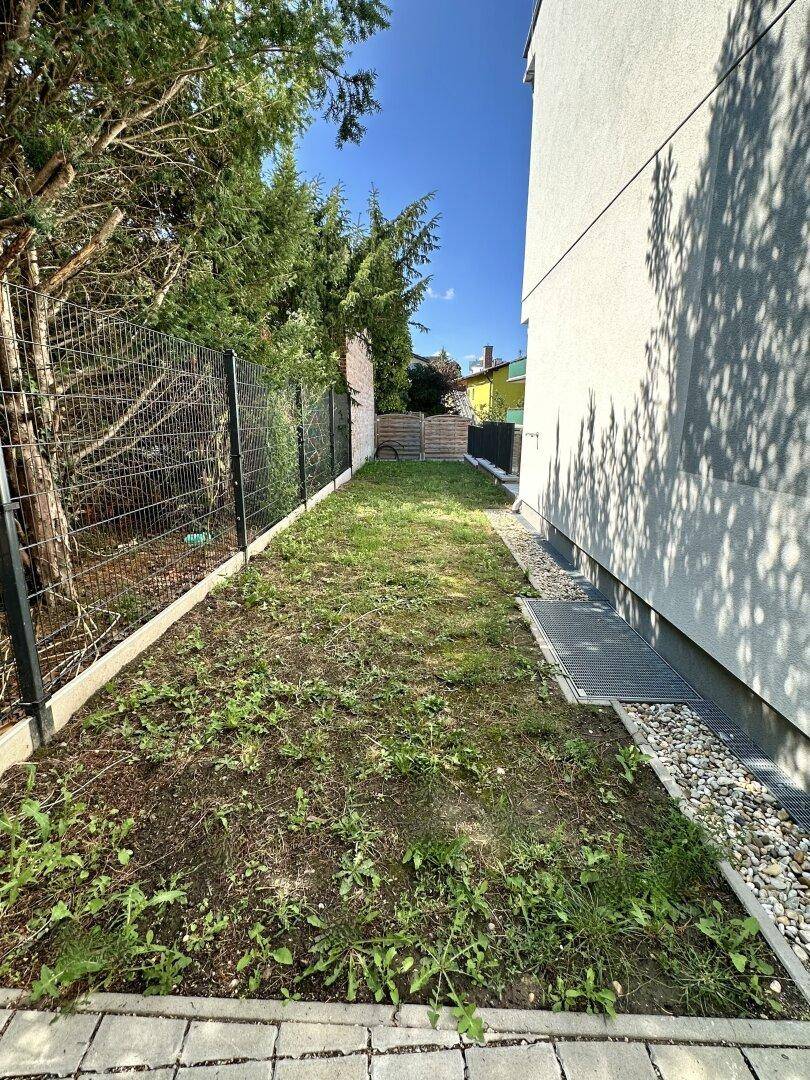 Schmaler Gartenstreifen entlang des Hauses mit Zaun und junger Bepflanzung, bereit zur Gestaltung.