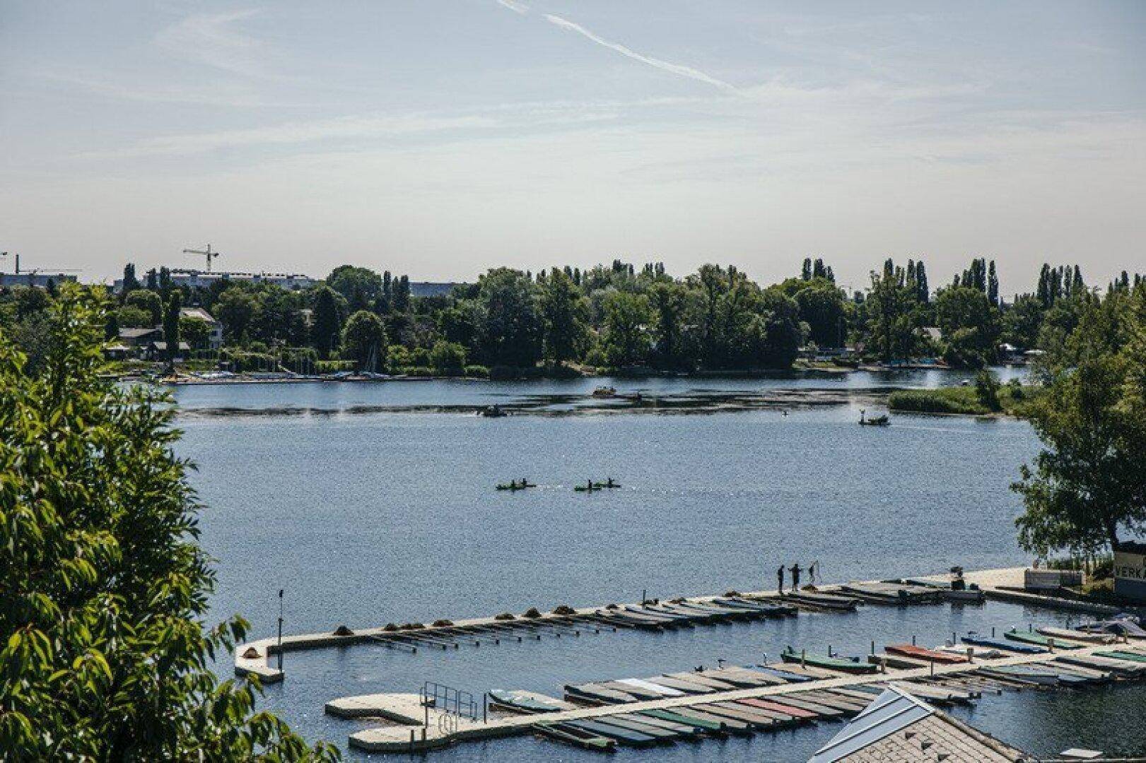 Malerischer Blick auf einen See mit zahlreichen Booten und grünen Ufern unter blauem Himmel.