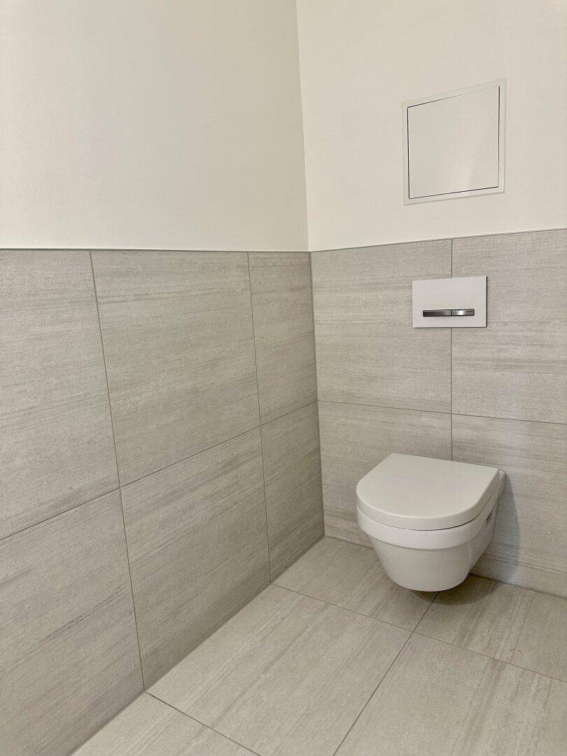 Modernes Gäste-WC mit wandhängender Toilette und stilvollen hellgrauen Wandfliesen.