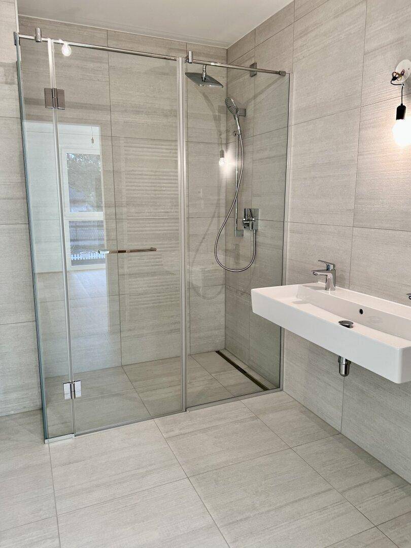 Modernes Badezimmer mit begehbarer Dusche, Einzelwaschbecken und hellgrauen Fliesen.