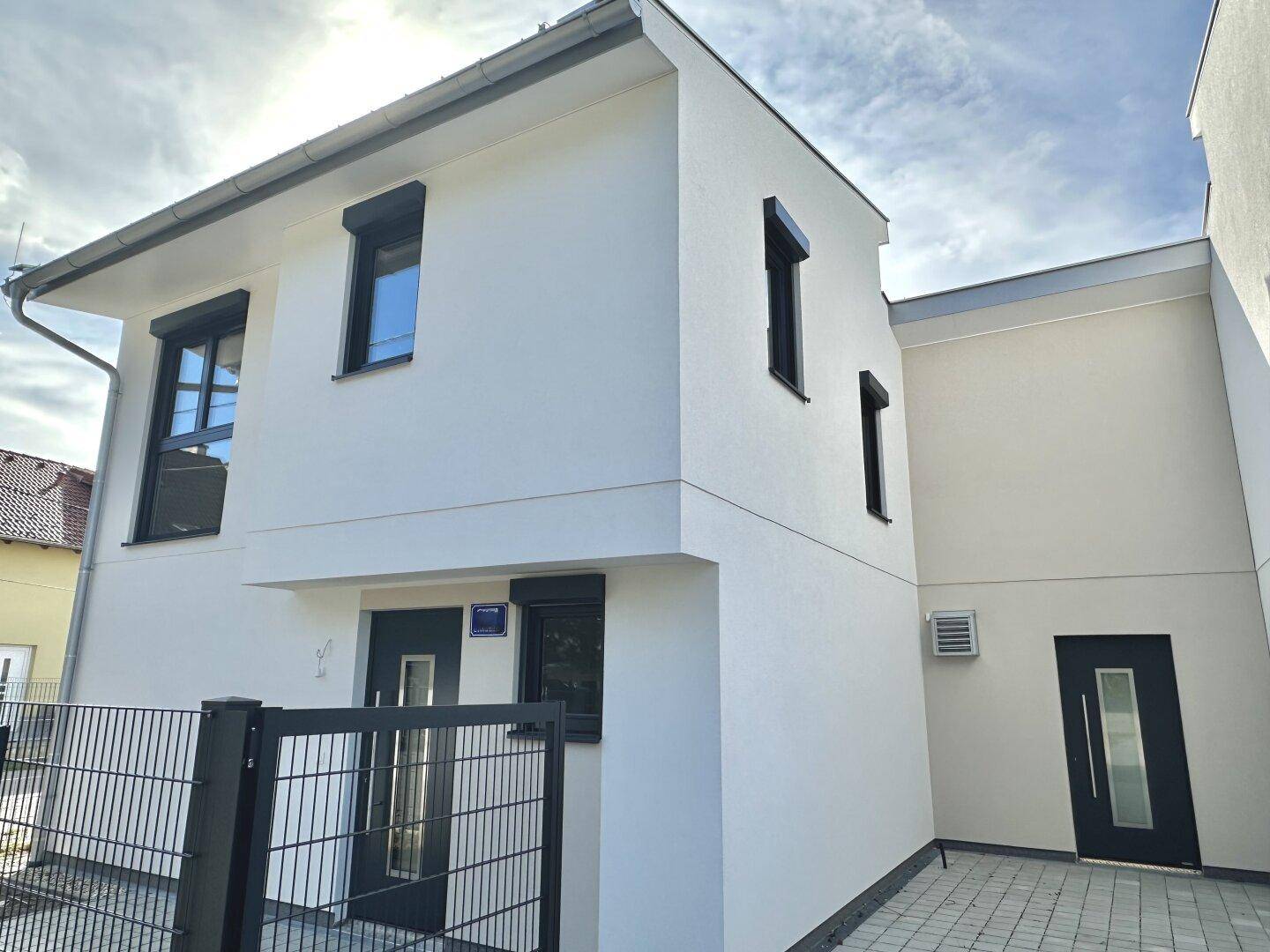 Moderne Hausfassade in Weiß mit schwarzen Fensterläden und Eingangstüren, ein Neubau.