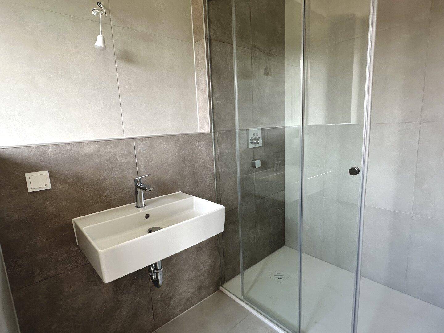 Zeitgemäßes Badezimmer mit rechteckigem Waschbecken und Duschkabine, in schlichten Grautönen gestaltet.