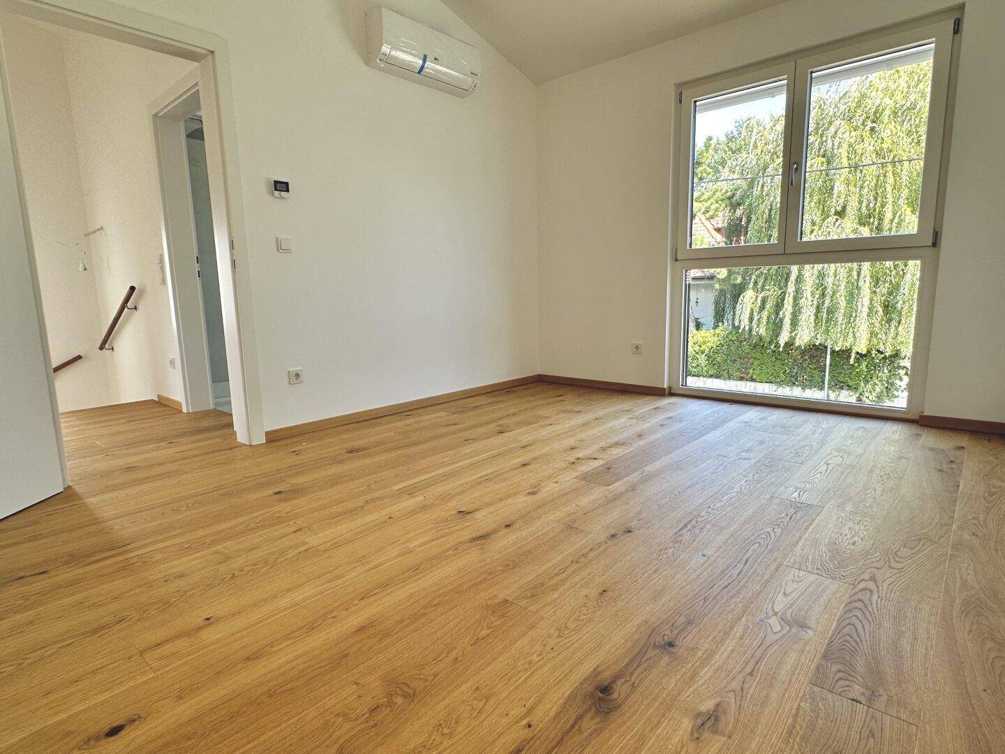 Helles Zimmer mit Holzfußboden, großen Fenstern und installierter Klimaanlage für Komfort.